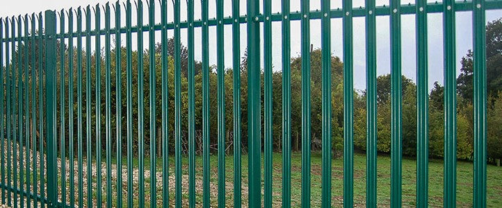 Green metal palisade fence with trees in the background