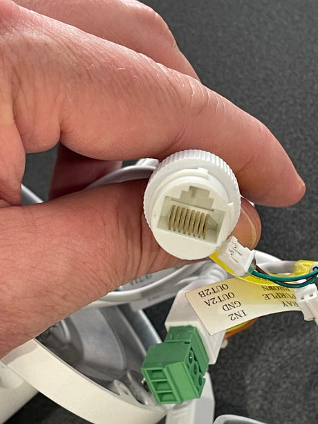 Hand holding a white electrical connector with green and yellow wires against a gray background