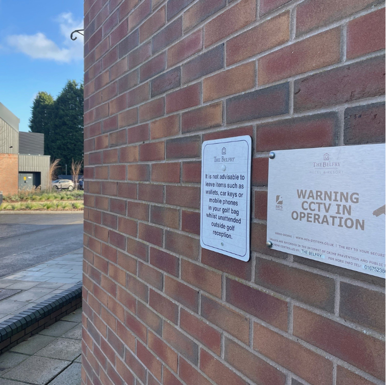 Brick wall with two signs, one warning of MES Systems CCTV operation.