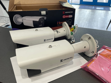 Two Hikmicro security cameras on a table with packaging in the background.
