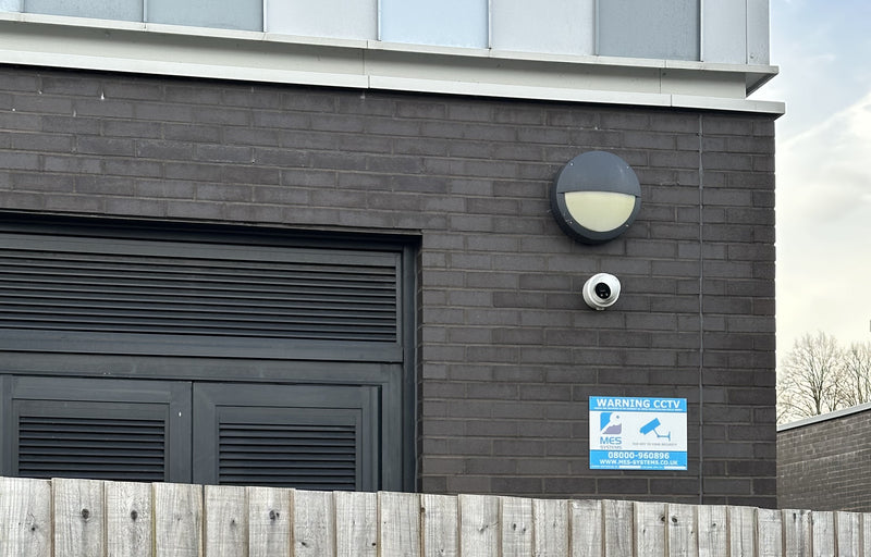 School building exterior with MES Systems security camera, warning sign, and light fixture.
