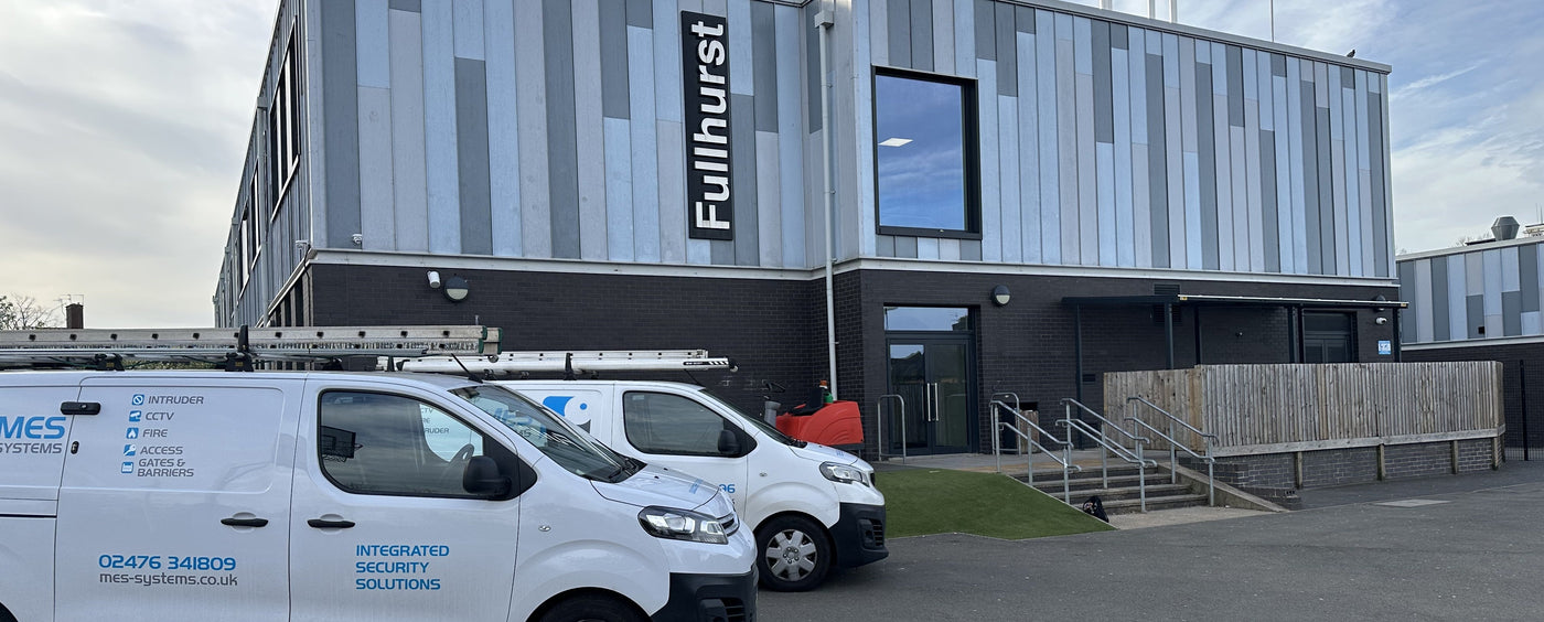 Two white vans MES vans, parked in front of a building with School fitting CCTV