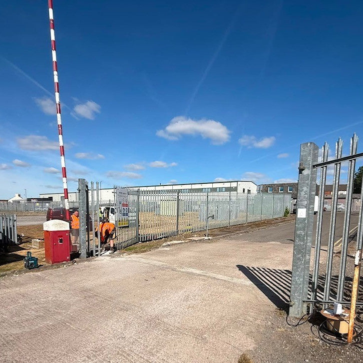 An outdoor industrial facility with a person standing near the gate.