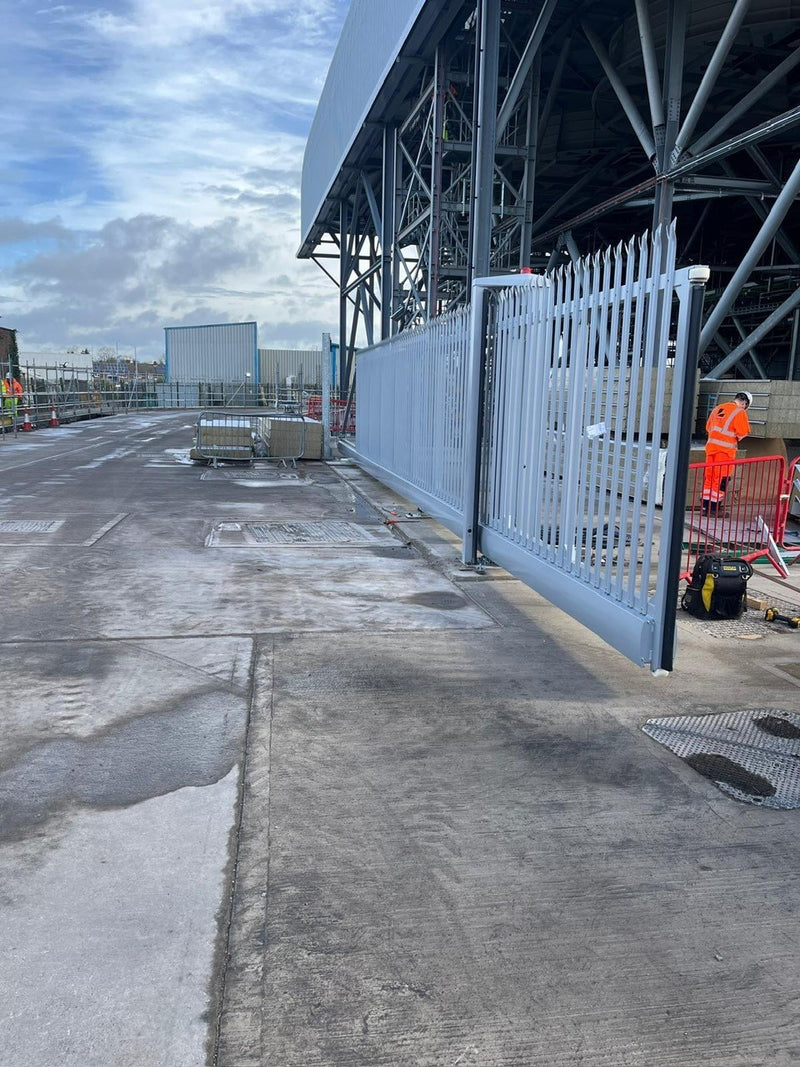 Automatic gates installed at energy-from-waste facility. Construction site with a large building under construction and workers in orange vests.