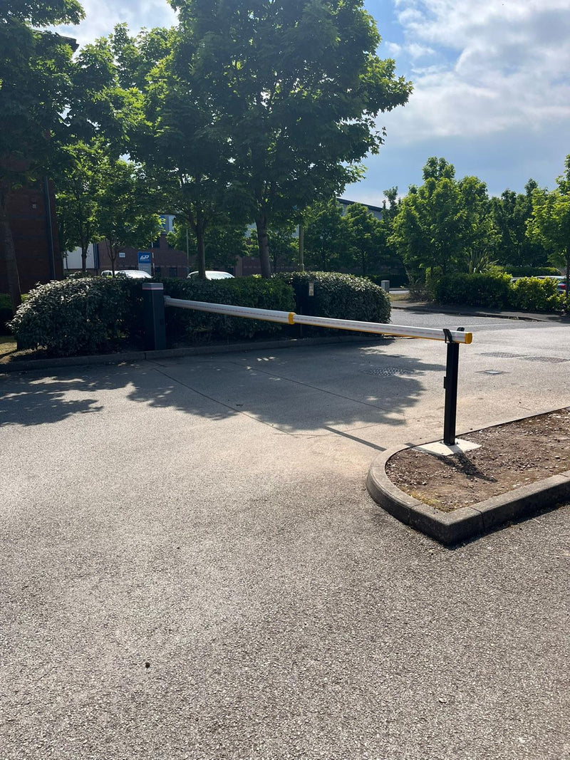 Driveway with a closed automatic gate, trees, and a clear sky.