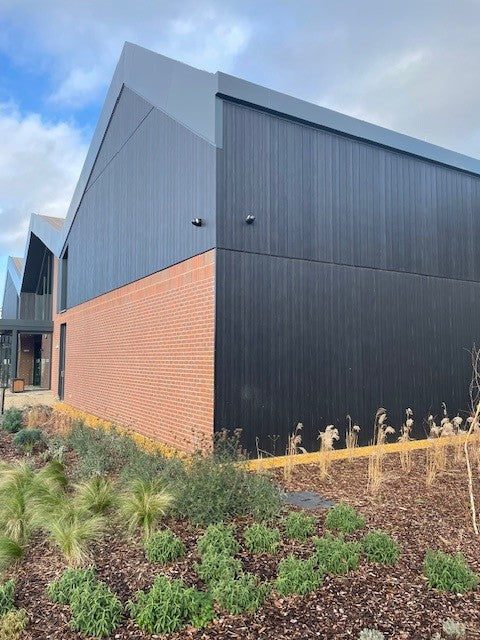 Modern building with a black and brick facade, surrounded by greenery and a clear sky. Black discreet CCTV camera 