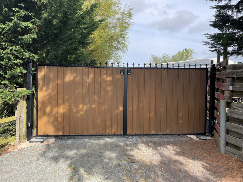 Wooden effect composite gate with black metal frame in a driveway setting