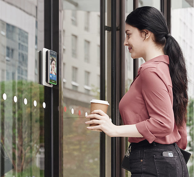Woman using a face recognition door opener with a coffee cup in an urban setting