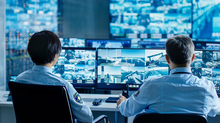 2 people infront of CCTV monitoring screens