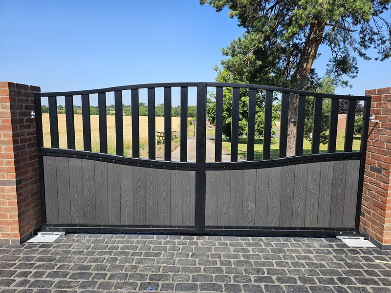 Black metal and grey wooden automatic gate with brick pillars at a residential property on a sunny day.