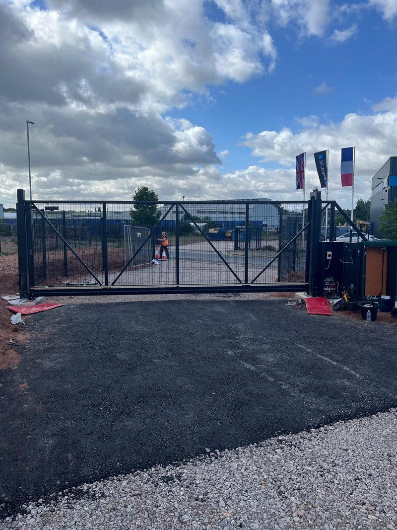 Black metal automatic gate at a commercial property with a cloudy sky above.