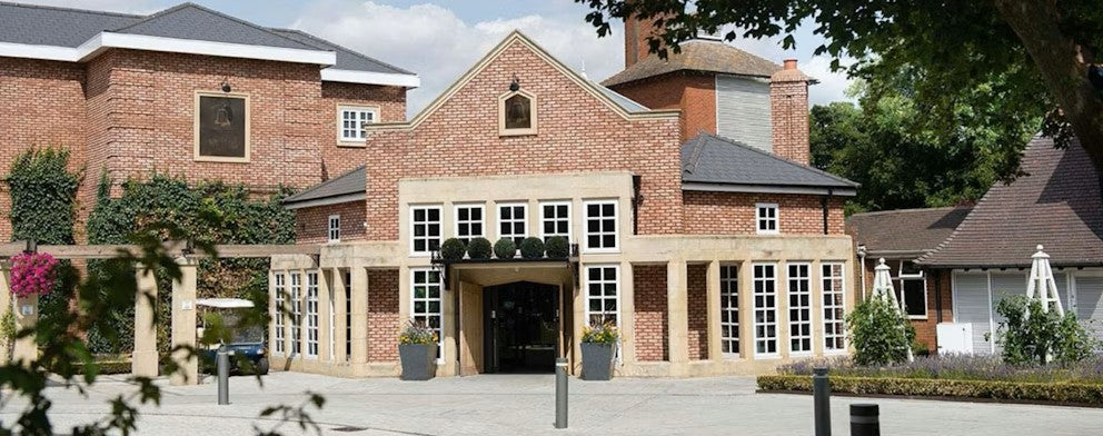 The Belfry Brick building with large windows and a driveway entrance, surrounded by trees and plants.